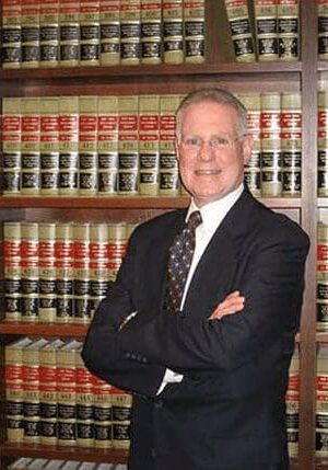 A man in suit and tie standing next to a book shelf.